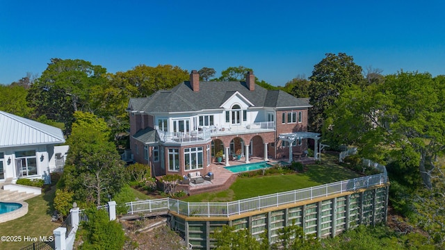 back of property with a chimney, a fenced backyard, a balcony, brick siding, and an outdoor pool