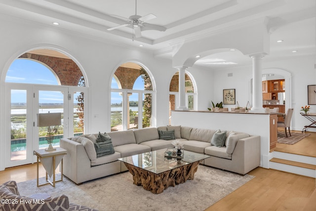living area with a wealth of natural light, a water view, and decorative columns