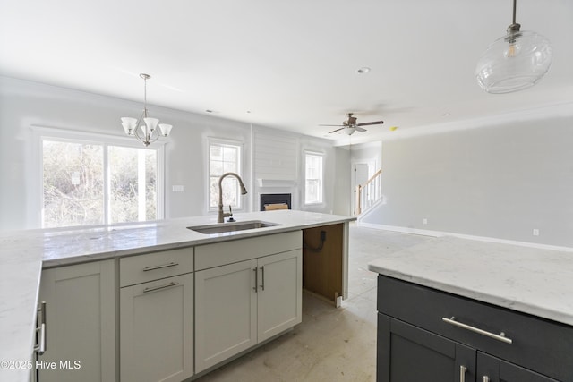 kitchen with gray cabinets, sink, light stone counters, and decorative light fixtures