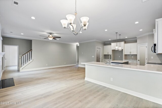 kitchen with crown molding, backsplash, white cabinets, light stone countertops, and light wood-type flooring