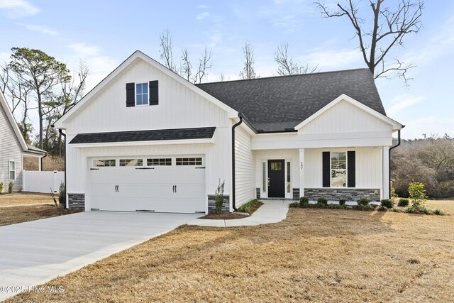 modern farmhouse style home with a garage, driveway, stone siding, roof with shingles, and a front yard