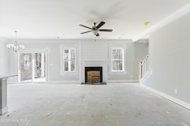 unfurnished living room featuring a fireplace, ceiling fan with notable chandelier, and a wealth of natural light