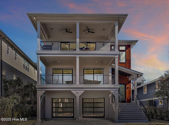 view of front of property featuring ceiling fan, a balcony, a garage, stairs, and stucco siding