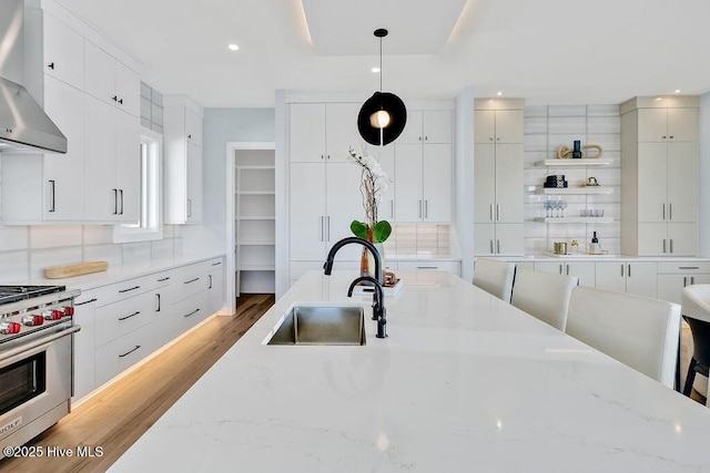 kitchen with light wood-style flooring, a sink, decorative backsplash, luxury stove, and wall chimney range hood