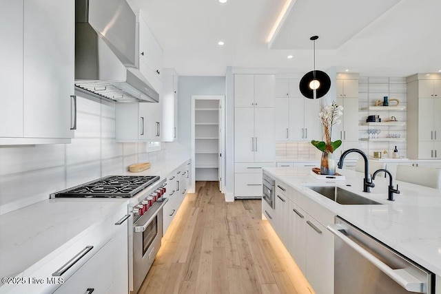 kitchen with recessed lighting, stainless steel appliances, a sink, wall chimney exhaust hood, and decorative backsplash