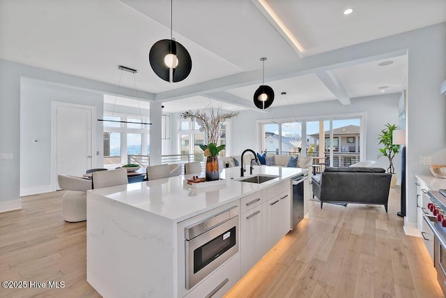 kitchen with a sink, open floor plan, light countertops, light wood-style flooring, and appliances with stainless steel finishes
