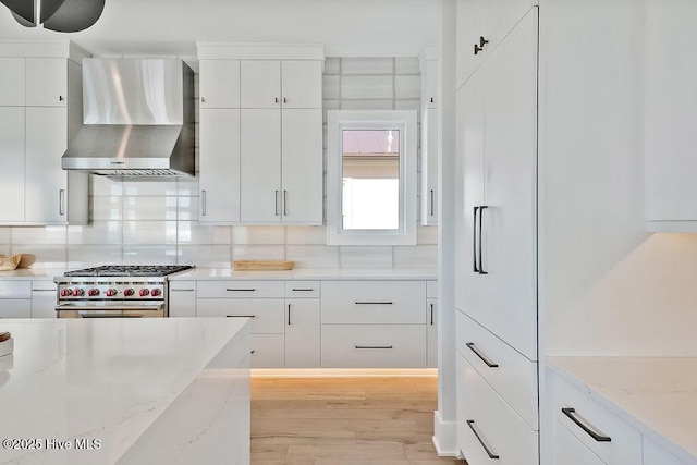 kitchen featuring wall chimney exhaust hood, high end stove, white cabinets, and light wood-type flooring