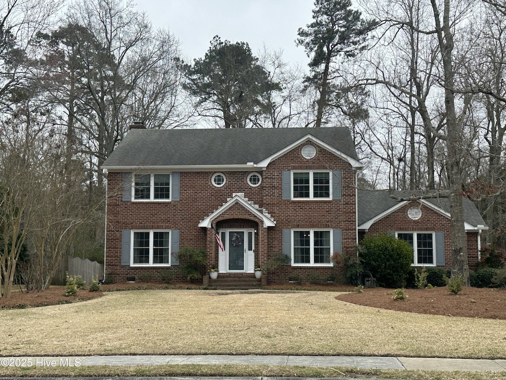 colonial home featuring brick siding, a chimney, a front yard, and fence