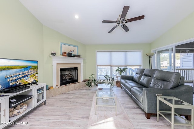 living room with a tiled fireplace, lofted ceiling, ceiling fan, and light hardwood / wood-style flooring