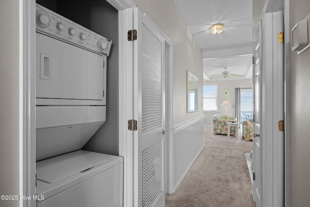 washroom featuring stacked washer / dryer, ceiling fan, light carpet, and a textured ceiling