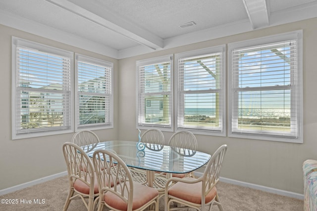 dining area with a textured ceiling, light colored carpet, and beamed ceiling