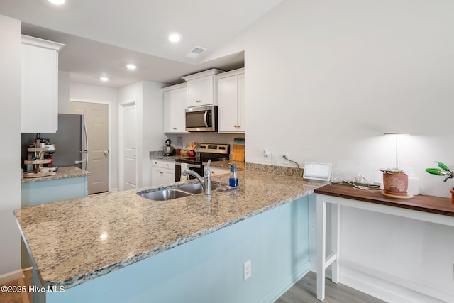 kitchen with sink, white cabinetry, stainless steel appliances, light stone countertops, and kitchen peninsula