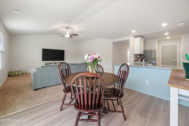 dining area featuring ceiling fan, lofted ceiling, sink, and light hardwood / wood-style flooring