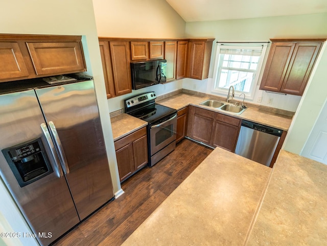 kitchen with brown cabinetry, a sink, dark wood finished floors, appliances with stainless steel finishes, and vaulted ceiling