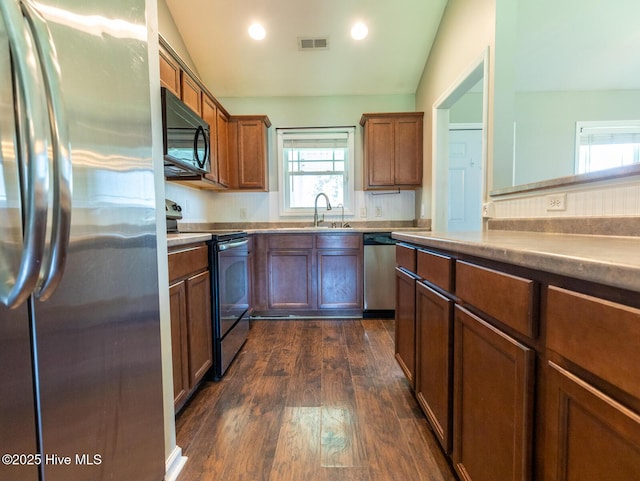 kitchen with dark wood-style flooring, appliances with stainless steel finishes, a sink, lofted ceiling, and visible vents