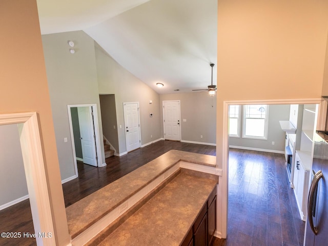 interior space featuring a ceiling fan, baseboards, dark wood-type flooring, and a towering ceiling