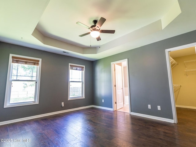 unfurnished bedroom featuring visible vents, wood finished floors, baseboards, a tray ceiling, and a spacious closet