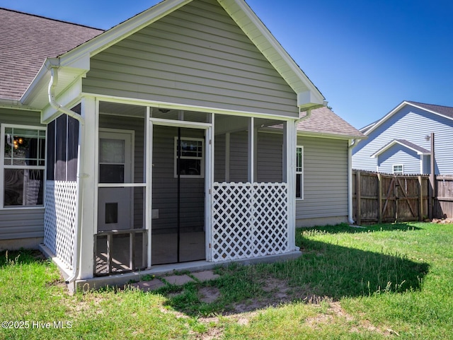 rear view of house featuring a sunroom, a lawn, fence, and roof with shingles