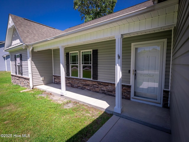 entrance to property with roof with shingles, covered porch, a lawn, and stone siding