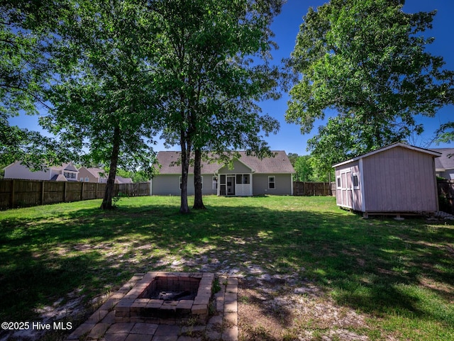 view of yard with a fenced backyard, a fire pit, a shed, and an outbuilding