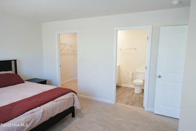 bedroom with light carpet, a spacious closet, a closet, and ensuite bathroom