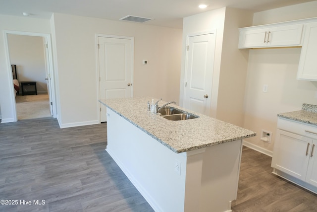 kitchen with white cabinetry, sink, light stone countertops, and an island with sink