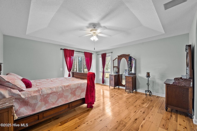 bedroom featuring ceiling fan, a tray ceiling, light hardwood / wood-style floors, and a textured ceiling