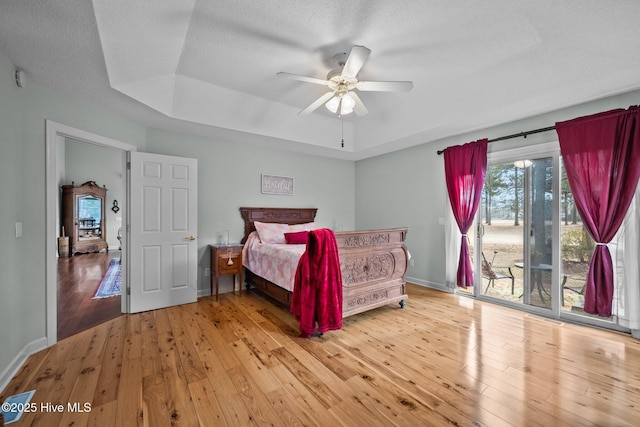 bedroom featuring a tray ceiling, access to exterior, ceiling fan, light hardwood / wood-style floors, and a textured ceiling