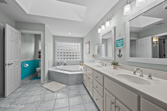 bathroom featuring vanity, a skylight, tiled bath, and toilet