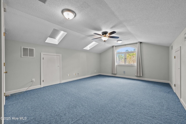 additional living space with ceiling fan, a textured ceiling, vaulted ceiling with skylight, and carpet flooring