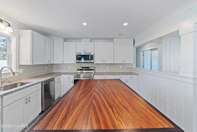 kitchen with appliances with stainless steel finishes, butcher block counters, sink, and white cabinets