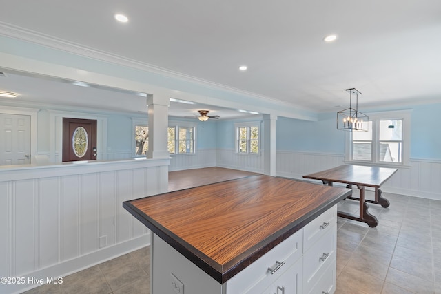 kitchen with light tile patterned floors, crown molding, white cabinets, a kitchen island, and decorative light fixtures