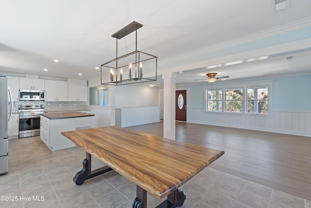 tiled dining area with ceiling fan and ornamental molding