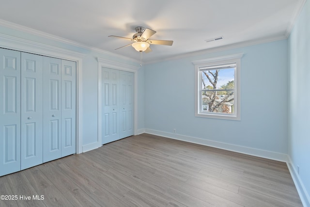 unfurnished bedroom with crown molding, two closets, light hardwood / wood-style flooring, and ceiling fan