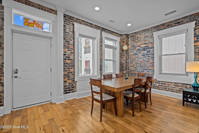 dining space with crown molding, light wood-type flooring, and brick wall