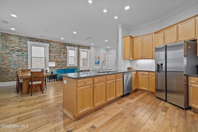 kitchen with appliances with stainless steel finishes, sink, dark stone countertops, ornamental molding, and kitchen peninsula