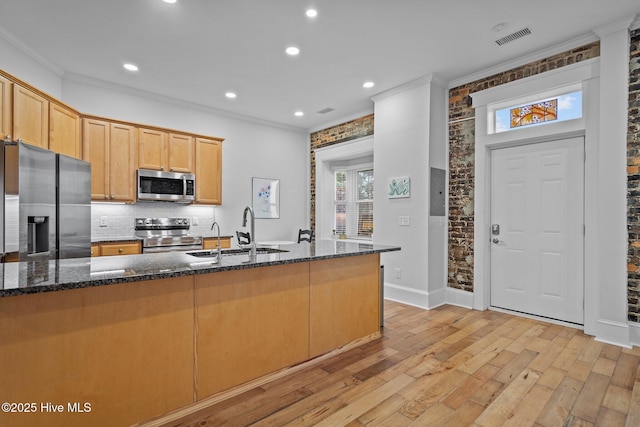 kitchen featuring sink, light wood-type flooring, dark stone countertops, appliances with stainless steel finishes, and brick wall