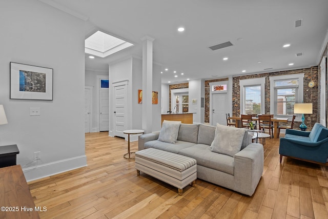 living room featuring ornamental molding, brick wall, light hardwood / wood-style floors, and a skylight