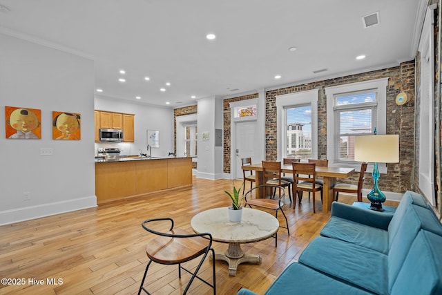 living room featuring sink, crown molding, light hardwood / wood-style floors, and brick wall