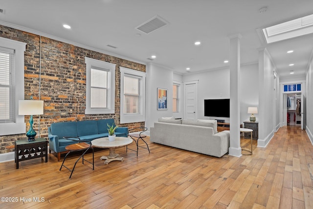 living room featuring a skylight, light wood-type flooring, ornamental molding, and brick wall