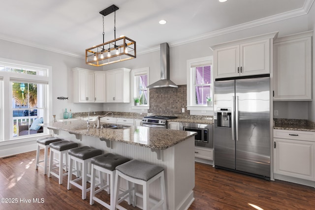 kitchen featuring wall chimney range hood, sink, stainless steel appliances, white cabinets, and a center island with sink