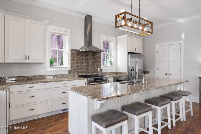 kitchen with white cabinets, a kitchen island with sink, light stone counters, stainless steel appliances, and wall chimney exhaust hood