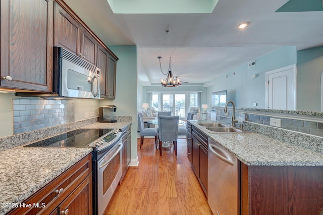 kitchen with light wood-style flooring, open floor plan, an inviting chandelier, stainless steel appliances, and a sink