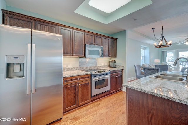 kitchen with light wood-style flooring, stainless steel appliances, a sink, open floor plan, and decorative backsplash