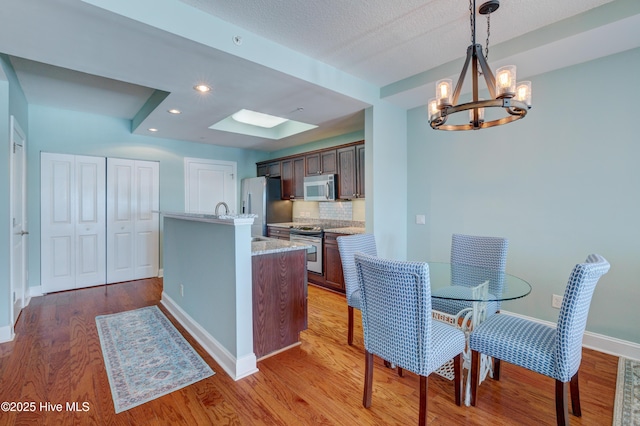 kitchen with light wood-style flooring, stainless steel appliances, dark brown cabinets, and decorative light fixtures