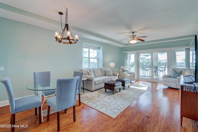 living area featuring ceiling fan with notable chandelier, a textured ceiling, baseboards, and wood finished floors