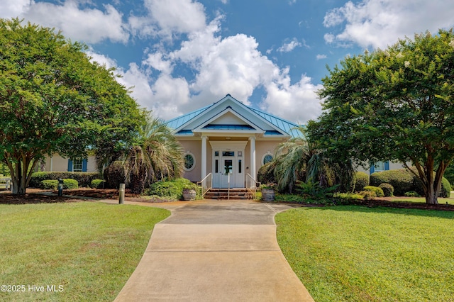 view of front facade with a standing seam roof, metal roof, stucco siding, and a front yard