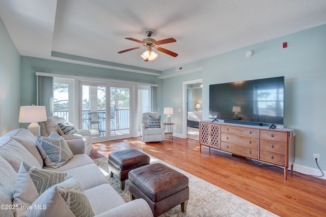living area with visible vents, wood finished floors, a ceiling fan, and baseboards