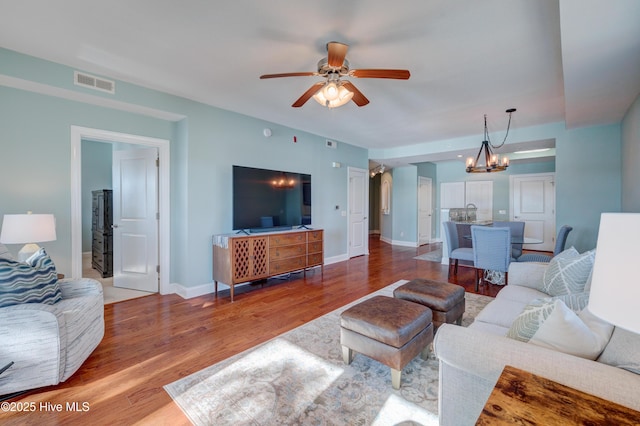 living area with ceiling fan with notable chandelier, visible vents, baseboards, and wood finished floors