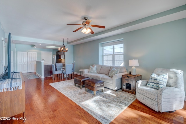 living area with ceiling fan with notable chandelier, baseboards, and wood finished floors